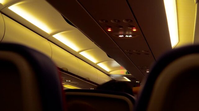 Night airplane cabin interior with passengers seated, overhead bins and ceiling lights creating warm dim travel atmosphere. In flight environment during night journey, economy class seating and quiet