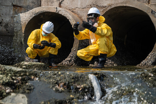 Environmental scientists in protective hazmat suits collecting water samples for pollution analysis and ecological research at an industrial site.