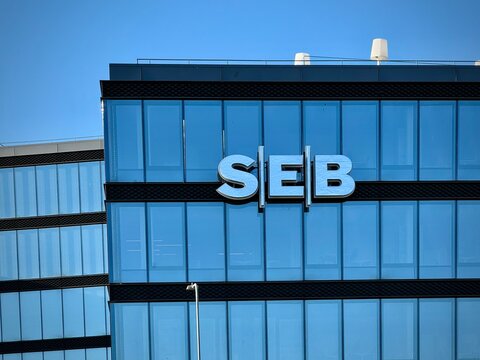 The SEB Bank logo on a building in Vilnius, Lithuania. The facade features large, reflective glass panels with a grid-like pattern. The logo consists of large, white letters 