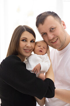 A smiling mother and father embrace their newborn baby, celebrating a new beginning together in a bright, indoor setting