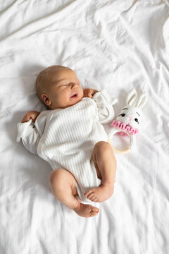 A peaceful newborn baby with closed eyes rests on a white textured blanket next to a cute bunny rattle