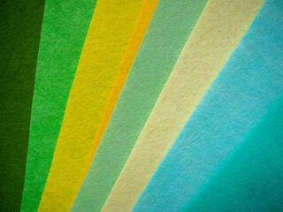 Fototapeta premium Multiple colorful felt fabric sheets fanned out diagonally displaying a nature-inspired color spectrum — dark forest green, bright green, yellow-green, golden amber, pale mint, cream/beige, light blue