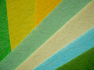 Fototapeta premium Multiple colorful felt fabric sheets fanned out diagonally displaying a nature-inspired color spectrum — dark forest green, bright green, yellow-green, golden amber, pale mint, cream/beige, light blue