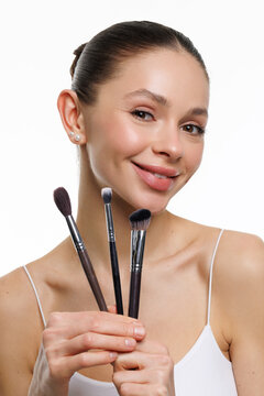 Beautiful woman with makeup brush on grey background