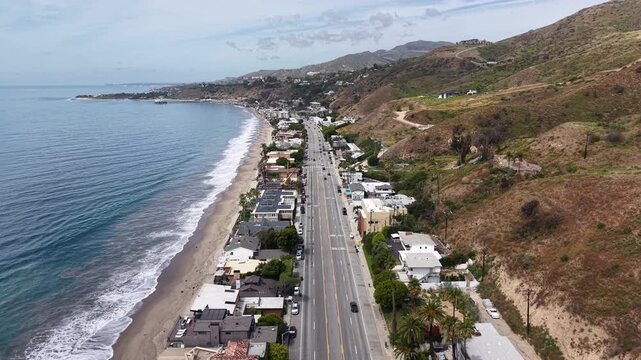 Cinematic 4K 10-bit aerial drone footage captured above the Pacific Coast Highway in Malibu, featuring a smooth forward dolly movement over vehicles traveling along the scenic coastal highway.