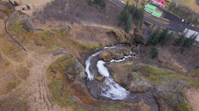 Systrafoss (Sister Falls) is a dual waterfall above the village of Kirkjub&aelig;jarklaustur, cascading over a steep mountain to the village below - tilt down aerial reveal