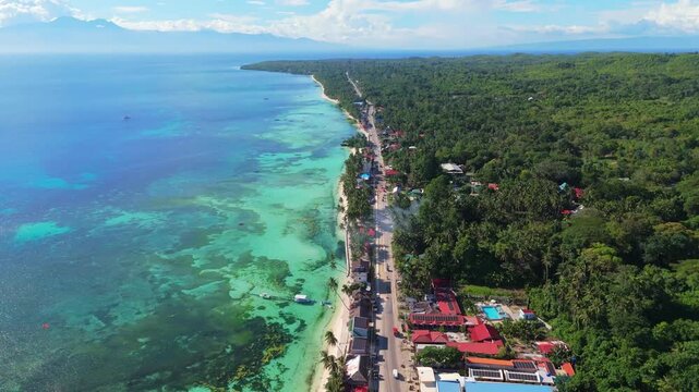 aerial view of San Juan coastline in Siquijor, Philippines. Crystal clear turquoise waters, coral reef, and white sand beach fringed by lush tropical palms and coastal resorts