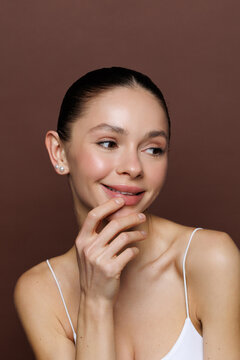 Young woman on a beige background. She has a delicate blush on her cheeks and painted lips.
