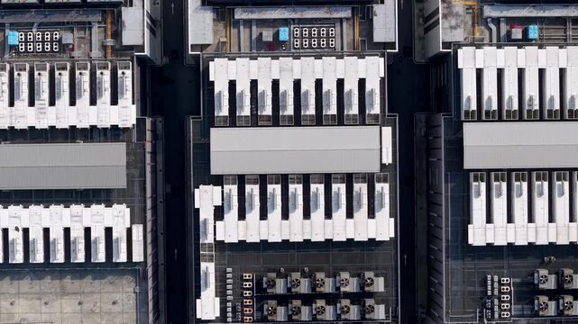 Aerial view of industrial rooftops. Rows of cooling units line the structures. Gray panels contrast with white mechanical arrays.