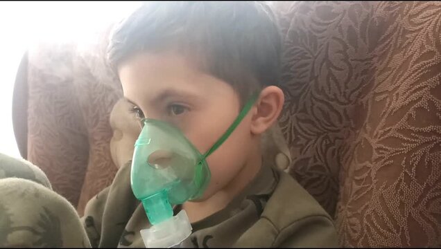 Boy using nebulizer with green mask for breathing treatment at home, child respiratory therapy, healthcare routine, medical care, illness recovery, pediatric treatment.