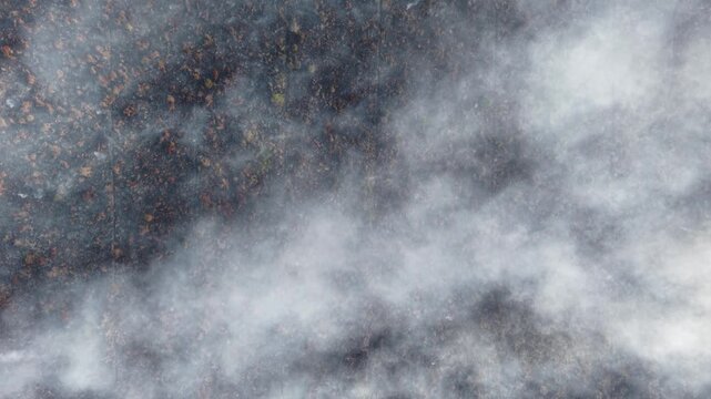 Drone aerial shot of smouldering peat soil with low smoke drifting across burned marshland.