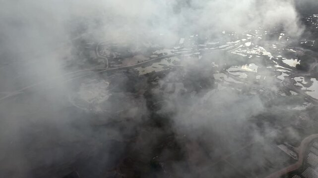Drone aerial of peat soil burning, dense smoke drifting over wetland waterlogged pits.