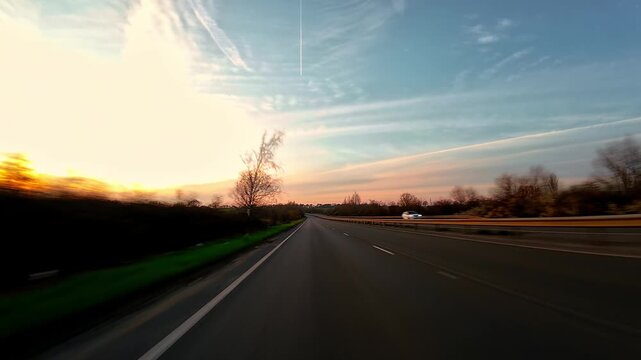 SUV traveling on open highway at sunset with wide sky and trees, rural driving journey first person view. Multi lane asphalt road stretching toward horizon with soft evening light, road trip driving