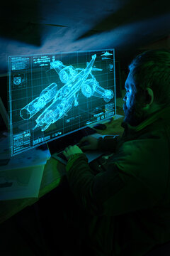 Engineer using laptop viewing military aircraft blueprint hologram in dark workspace. Concept of defense systems development, digital engineering, aerospace research and high tech innovation process.