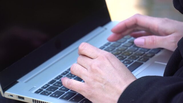 Woman's hands with stylish manicure rapidly typing on laptop keyboard outdoors, screen copy space