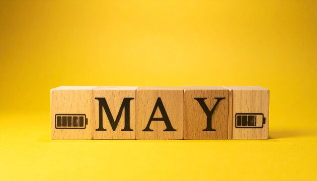 Four wooden blocks on bright yellow background spelling &ldquo;MAAY,&rdquo; second block with green triangular pyramid design, creative playful composition symbolizing identity, emphasis, and artistic interpretat