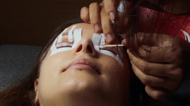 Cliente receiving a beauty treatment at a spa, with an esthetician applying products to curled eyelashes using a cotton swab for a lash lamination or perming procedure
