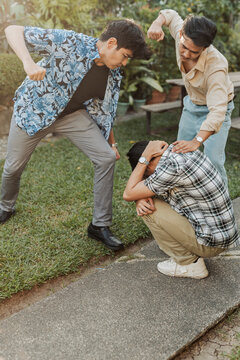 A frightened young Asian man shielding himself from two aggressive attackers during a violent confrontation in a tense outdoor setting. Outdoor shot.