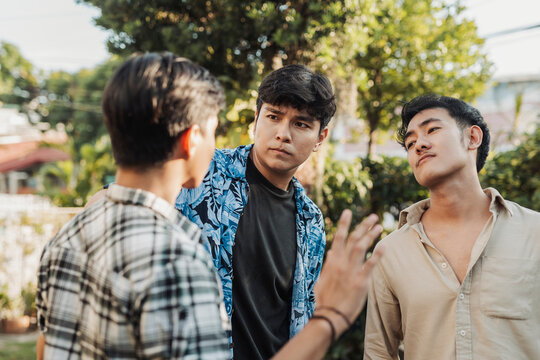 A anxious young Asian man trying to pacify two aggressive and hotheaded men during a tense argument. Outdoor shot.