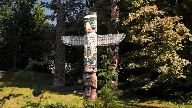 Sunlit totem pole in Stanley Park Vancouver colorful first nations carving among cedar trees and shaded lawn, intricate paintwork and weathered wood textures, Canada