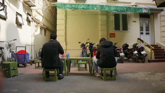 Customers eating lunch at authentic vietnamese food stall on typical narrow street in Hanoi, Vietnam, showing local urban culture and street dining tradition