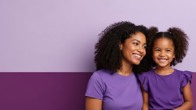 Smiling Black mother and daughter in purple shirts pose against a lavender and purple background.