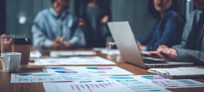 The Team Meeting Around a Table with Charts, Laptop, Coffee and Notebooks