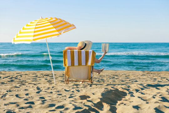 Woman reading book under beach umbrella by the sea