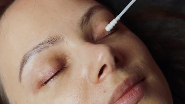 Woman receiving professional eyelash and eyelid cleansing with cotton swab by technician in salon, close up beauty treatment focused on hygiene, skin care and gentle cosmetic preparation