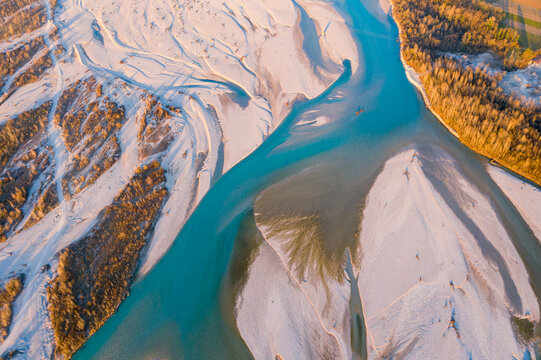 Aerial view of the braided Tagliamento river with turquoise water and white gravel banks under golden hour light Friuli-Venezia Giulia, Italy.