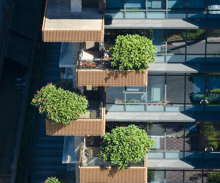 Aerial view of a modern residential building featuring wooden slat balconies with lush green trees and glass windows in Taiwan.