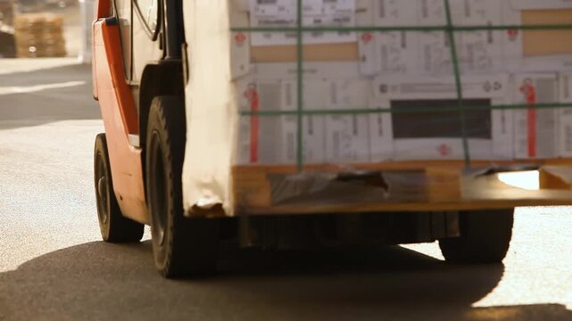 A forklift carries boxes through an outdoors warehouse. A forklift transports goods through an outdoors warehouse. Storage yard, warehouse yard. Finished factory products in boxes on pallets