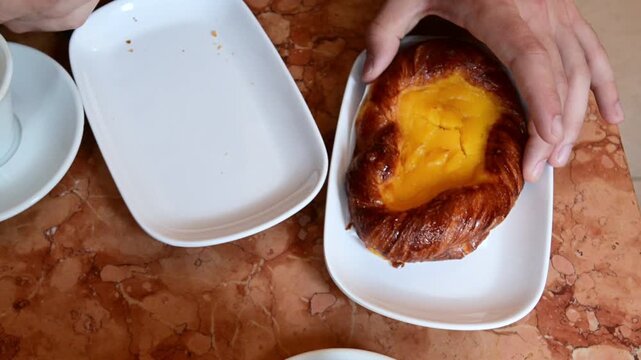 Top down slow motion view of a hand serving a traditional italian brioche with custard cream on a marble table in a cafe, representing the classic italian breakfast or colazione