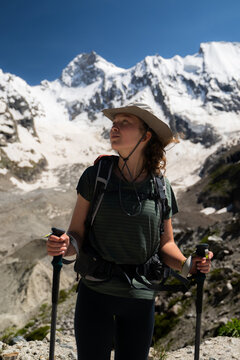 Portrait of a young woman hiker with trekking poles and a backpack in the snowy mountains during the day, acclimatizing before climbing.