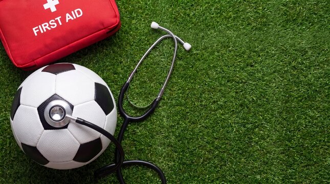 Soccer ball and first aid kit with stethoscope on green grass, sports medicine concept, athletic healthcare, injury prevention.