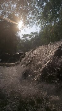 Slow motion of Sunlit waterfall cascading through a lush forest, creating a serene and tranquil natural scene.