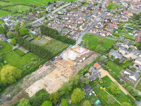 Interesting drone UAV view of a small, select housing development site at the edge of a Cambridgeshire, UK village. Currently archeology digs are seen on the left side of the building site.