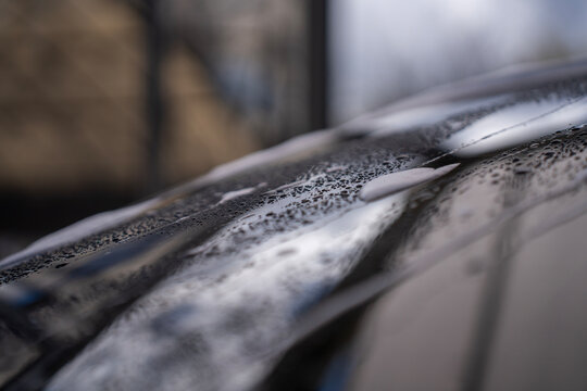 Close-up of water droplets and foam residue on a dark passenger car surface after washing at a self service car wash.
