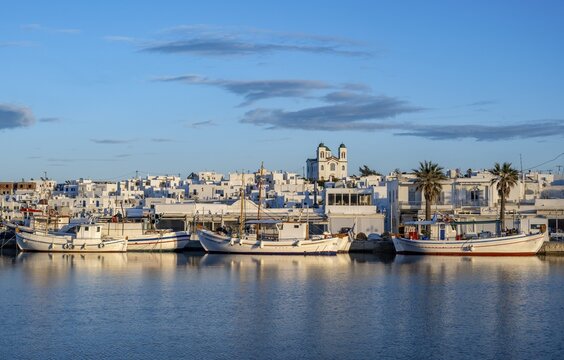 View of Naoussa, Fishing boats in the harbour at sunset, reflected in the sea, White Cycladic houses and church Agios Faneromeni, Naoussa, Paros, Cyclades, Greece