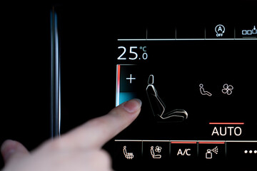 Finger touching touchscreen climate control to adjust front seat temperature setting in a modern...