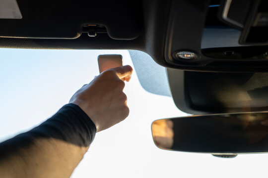 Hand holding toll transponder mounted on sun visor in modern car interior, close-up of electronic toll payment device near windshield.