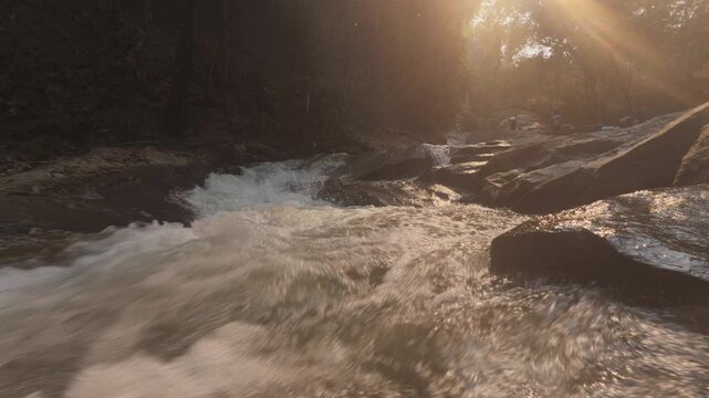 A tranquil scene of river rapids cascading over rocks, bathed in warm sunset light filtering through the surrounding trees.