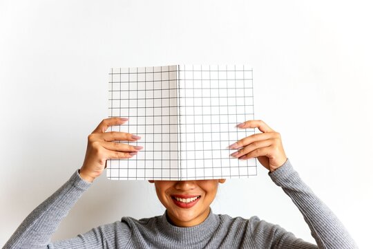Smiling woman hiding behind notebook.