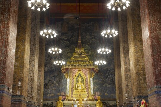 Golden meditating Buddha surrounded by wall paintings with Buddhist teachings and representations of Buddha's disciples, Wat Makut Kasatriyaram Ratchaworavihan, Phra Nakhon District, Old Bangkok, Thailand
