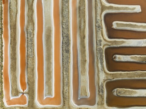 Saline ponds at the salt works near Chiclana de la Frontera. The orange-red colour depends on the level of salinity and is directly caused by the algae Dunaliella salina and brine shrimp. Aerial view. Drone shot. C&aacute;diz province, Andalusia, Spain