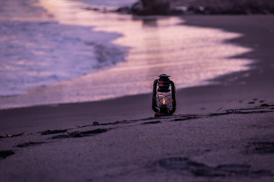 夕暮れの砂浜に置かれたアンティークなハリケーンランタン
