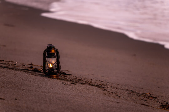 夕暮れの砂浜に置かれたアンティークなハリケーンランタン
