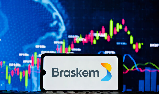 Braskem logo on a smartphone screen with a stock chart in the background. Braskem signed a contract to sell control of the company.