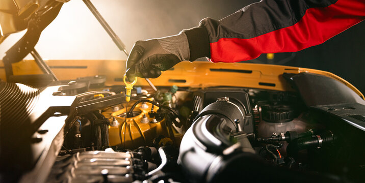 Mechanic checking engine oil level with dipstick in car engine. Automotive maintenance, inspection and professional service concept in workshop.