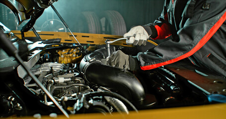 Fototapeta premium Mechanic repairing car engine in workshop, using tools with dramatic lighting. Automotive maintenance and professional service concept.